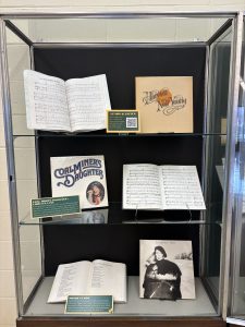 Vertical exhibit case with album records by Farm Aid 1985 artists, scores open to the music for songs performed at the concert, and a book of lyrics by Bob Dylan.