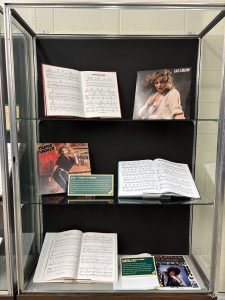 Vertical exhibit case with album records by Farm Aid 1985 artists and scores open to the music for songs performed at the concert.