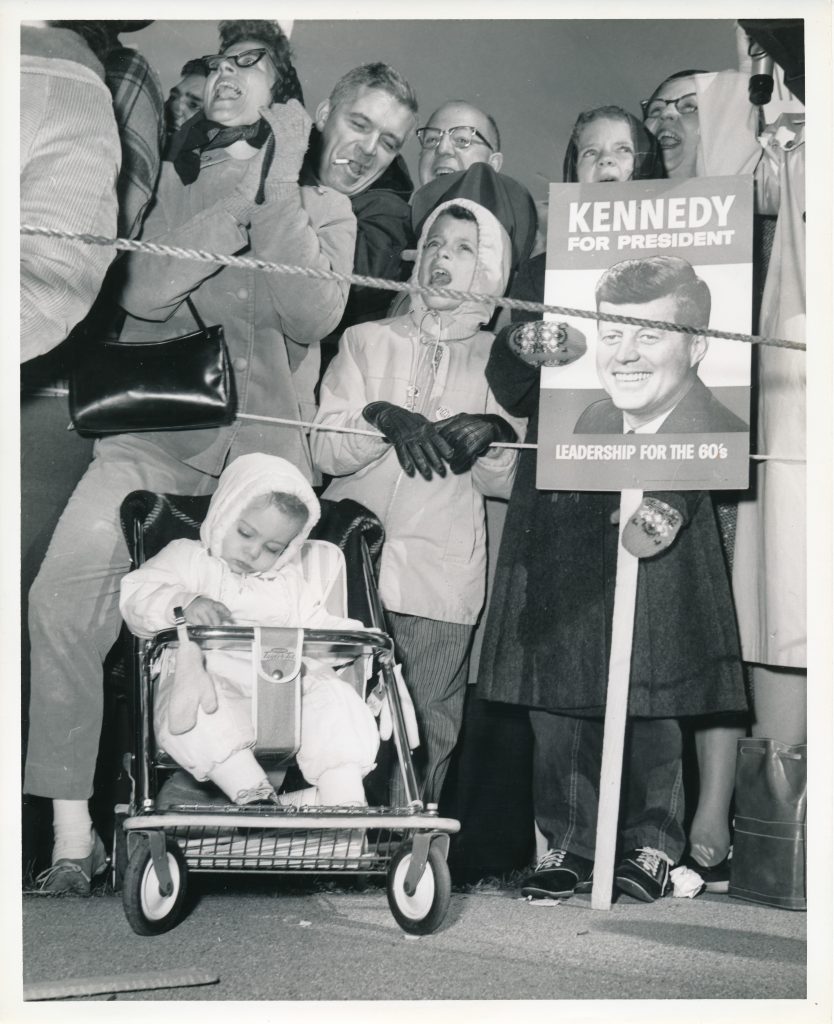 Men, women, and children gathered at Willard Airport to greet John F. Kennedy when he arrived.